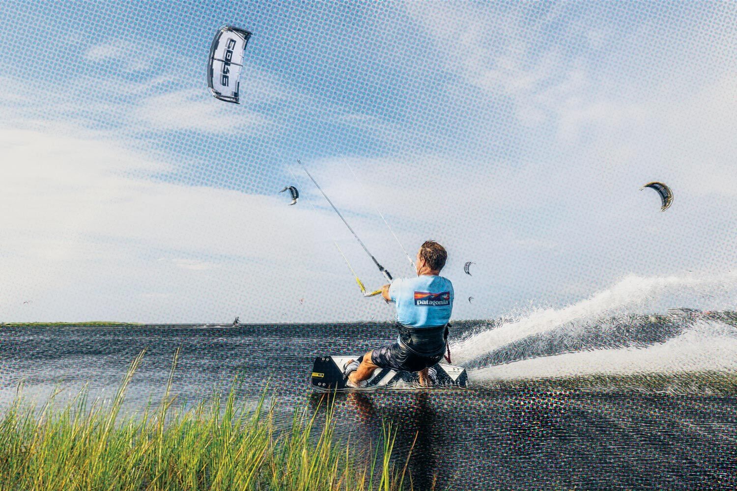 A man kiteboarding through the water, on Hatteras Island in North Carolina, with green reeds in the foreground