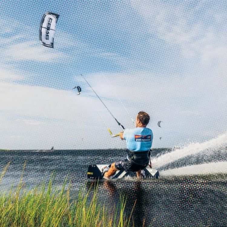 A man kiteboarding through the water, on Hatteras Island in North Carolina, with green reeds in the foreground