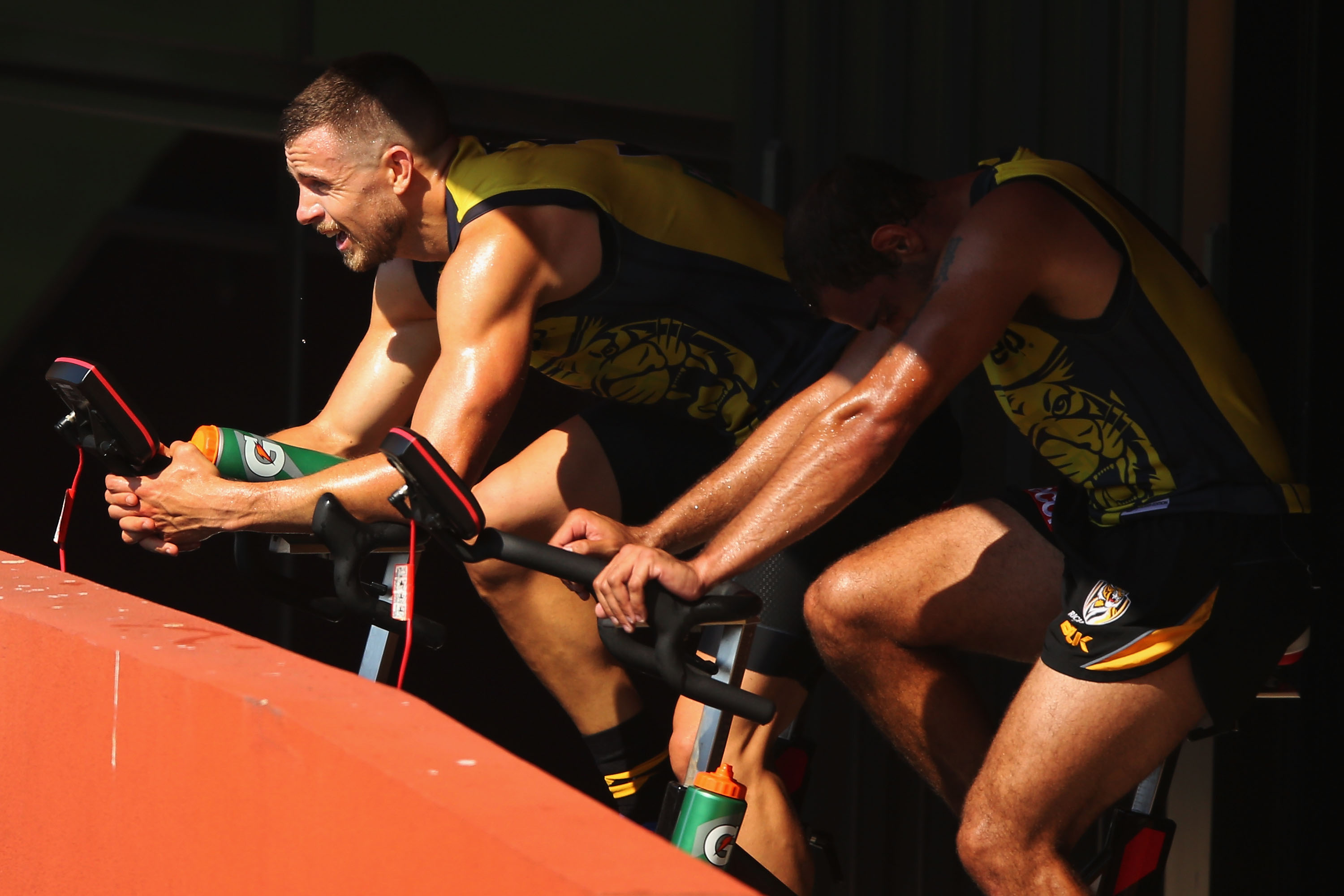 A pair of athletes on exercise bikes, drenched in sweat.