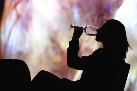 a silhouette of a woman drinking wine in front of a colorful screen