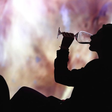 a silhouette of a woman drinking wine in front of a colorful screen