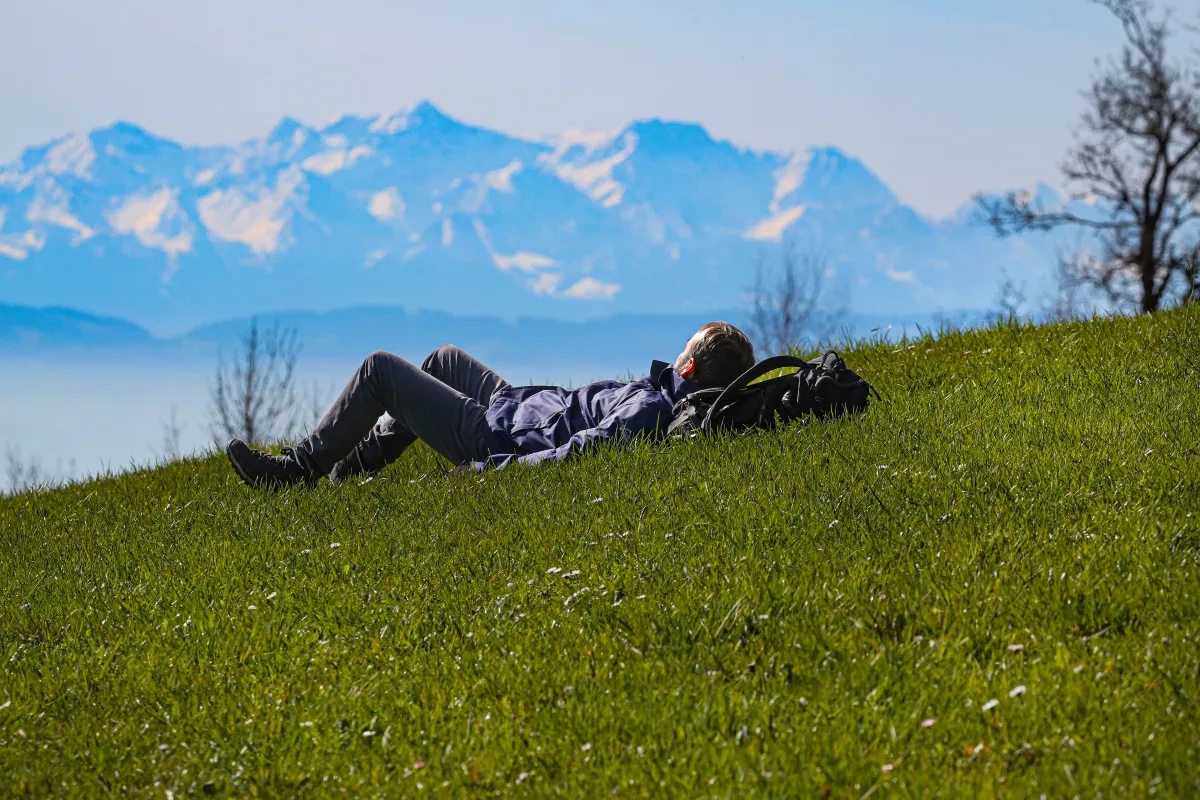 A man laying in the grass with mountains in the distance. The 20-5-3 Rule suggests spending more time in nature.