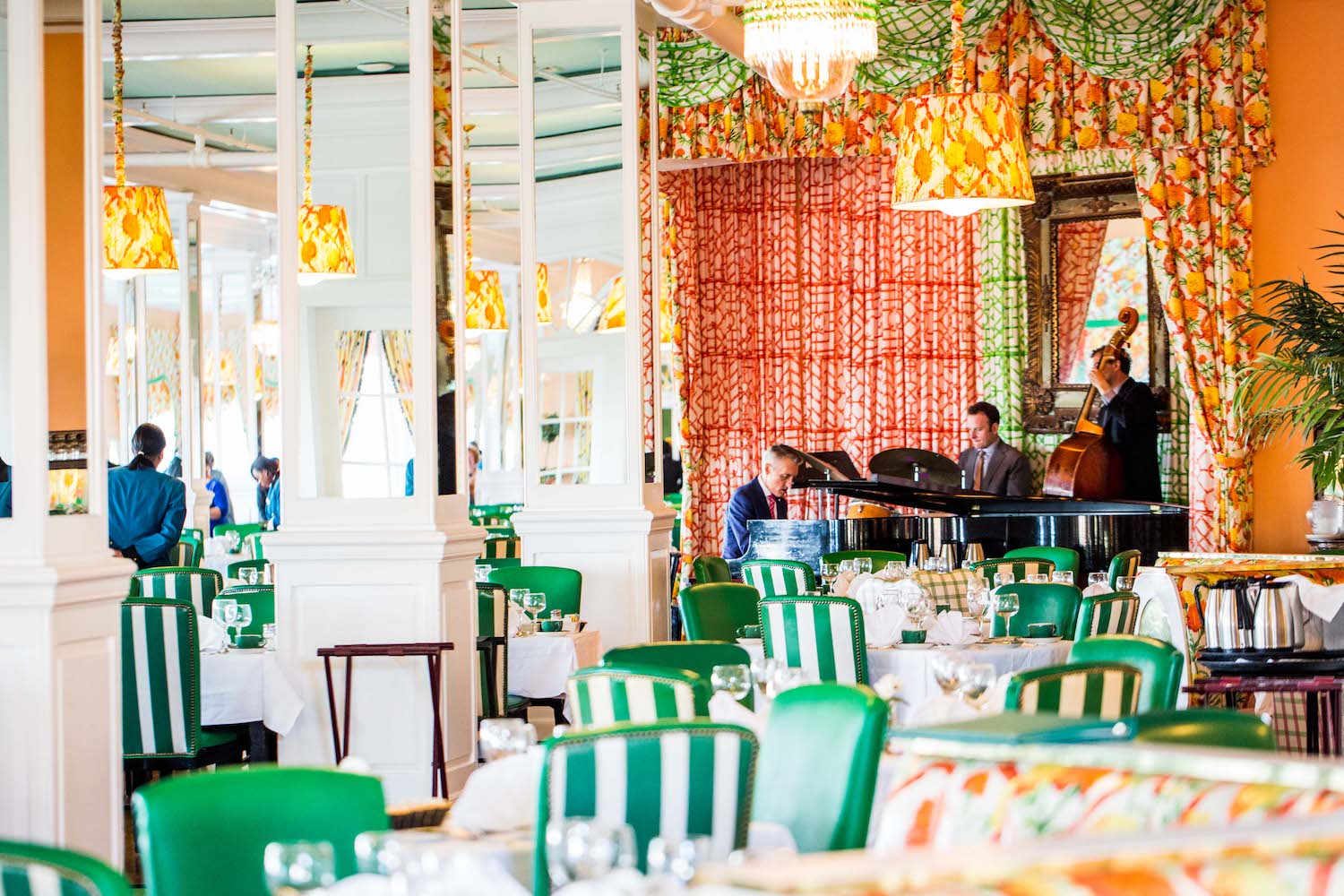 a dining room with orange walls, mirrored columns and green and white striped chairs