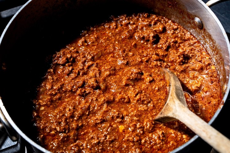 a big metal pot of meat chili with a wooden spoon sticking out