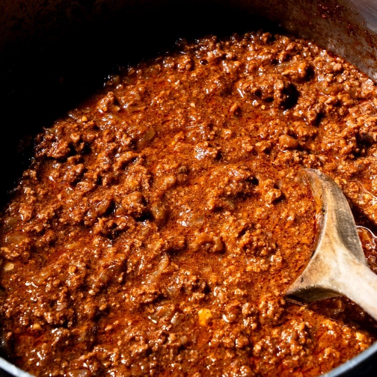 a big metal pot of meat chili with a wooden spoon sticking out