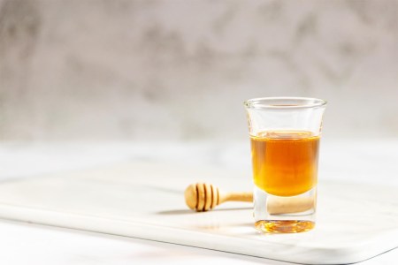 Honey shot and wooden dipper on marble tray with light gray background and copy space