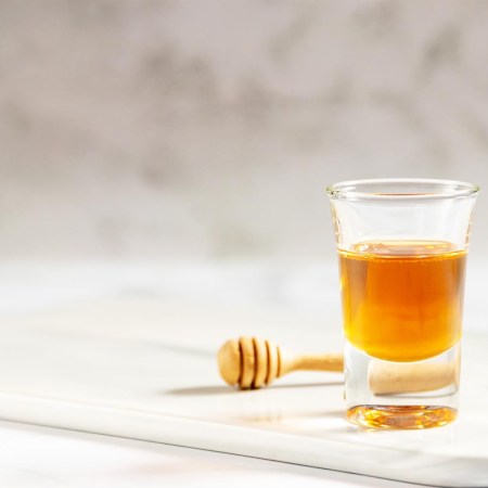 Honey shot and wooden dipper on marble tray with light gray background and copy space