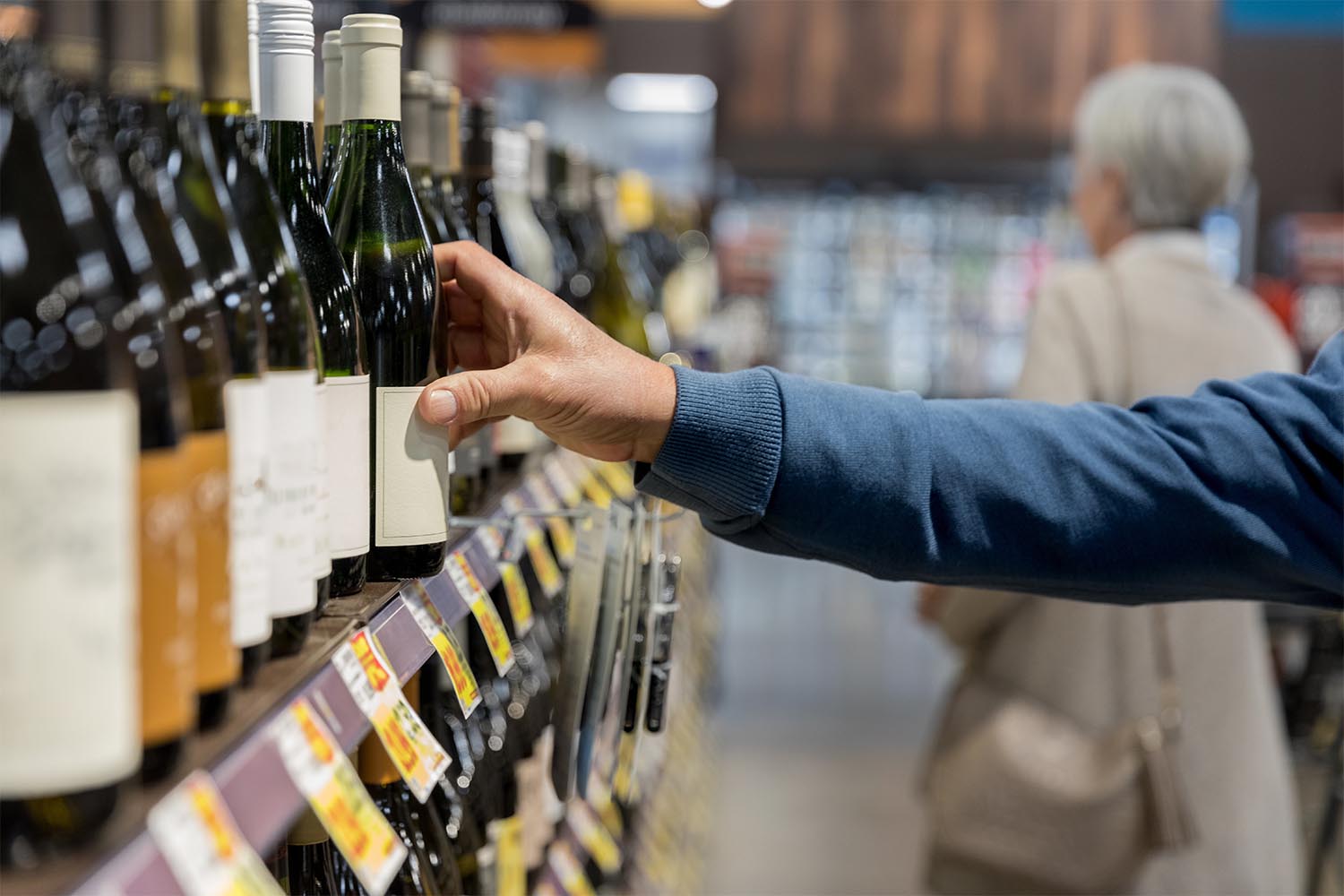 A man's arm reaching for a bottle of wine in a liquor store.