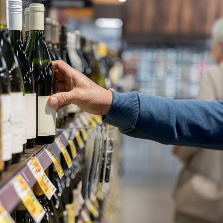 A man's arm reaching for a bottle of wine in a liquor store.