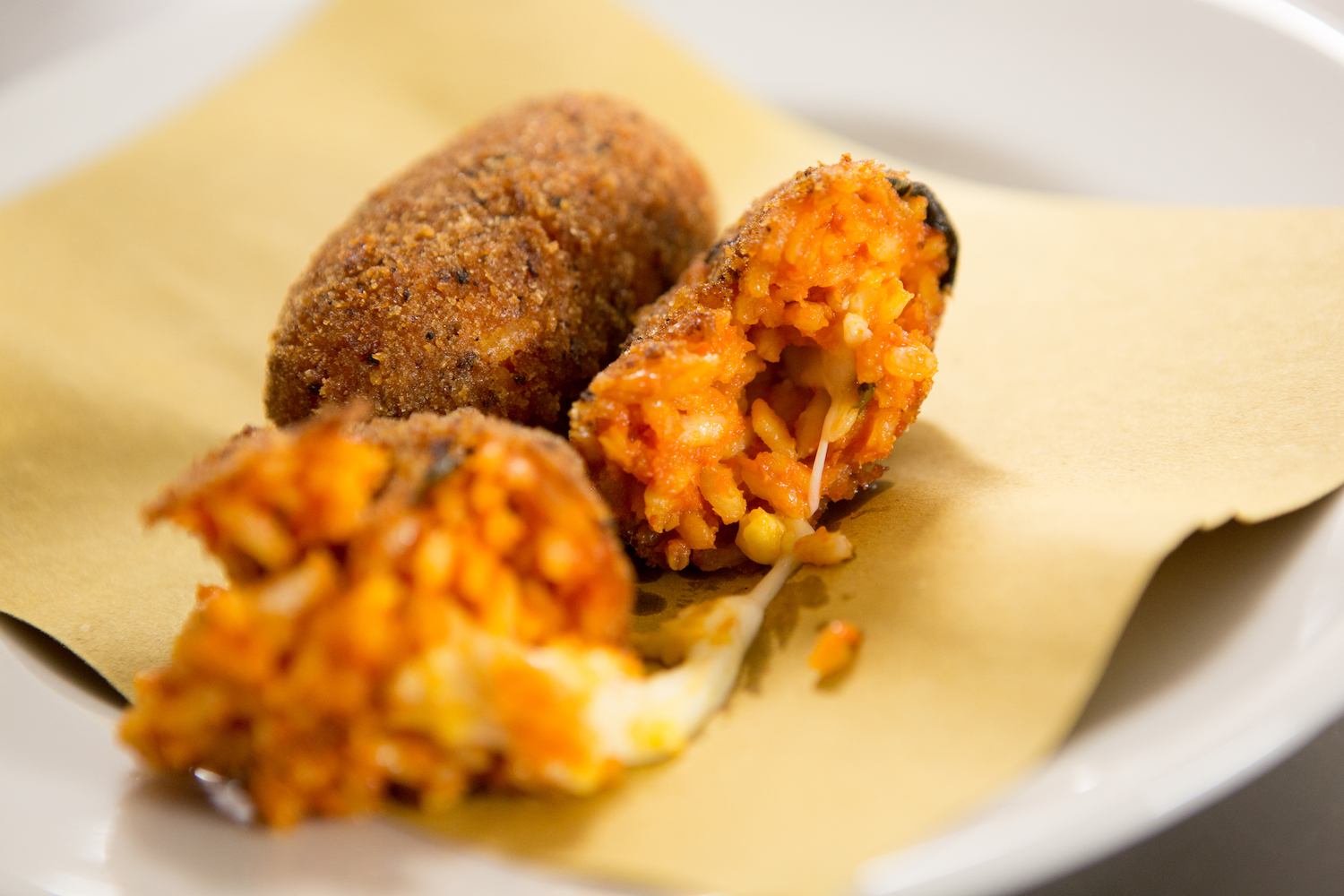 2 Suppli sitting on a piece of brown paper on a white plate