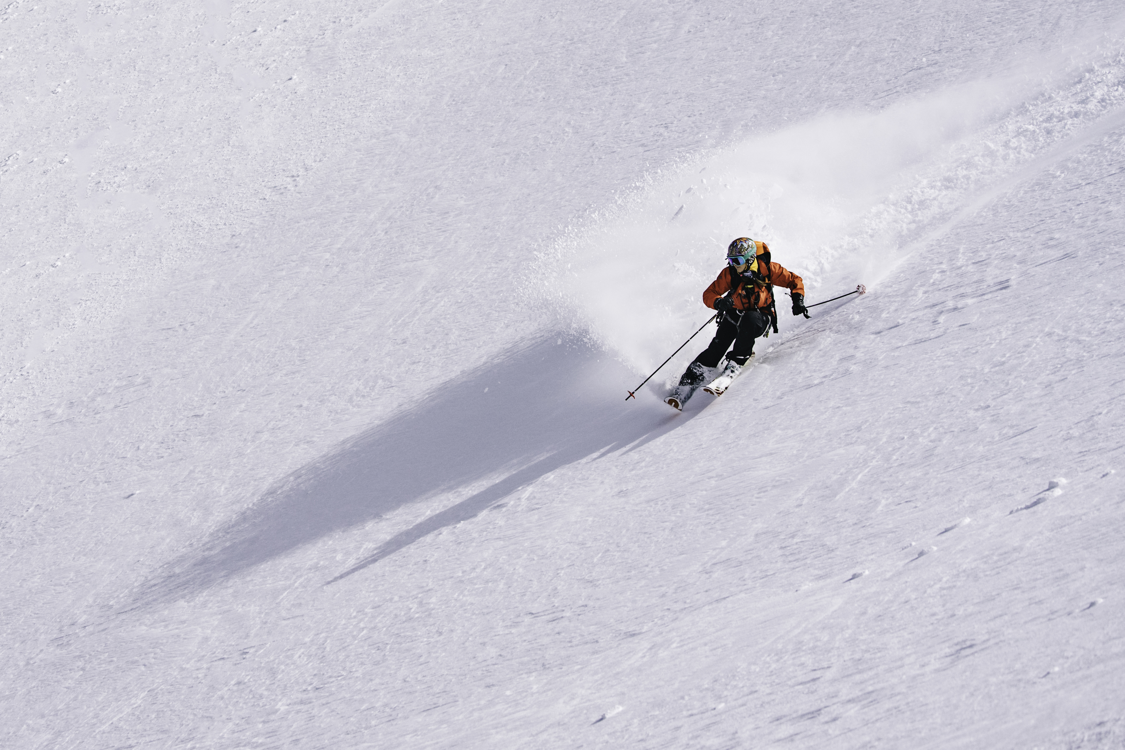 A skier carves into the snow, leaving a spray of snow in their wake.