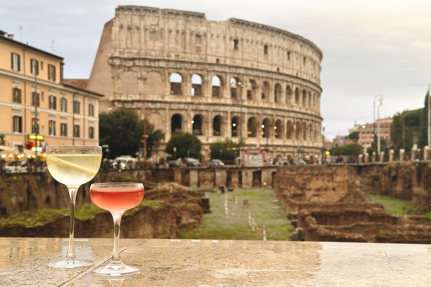 a martini and rd cocktail on a wet ledge overlooking the colosseum