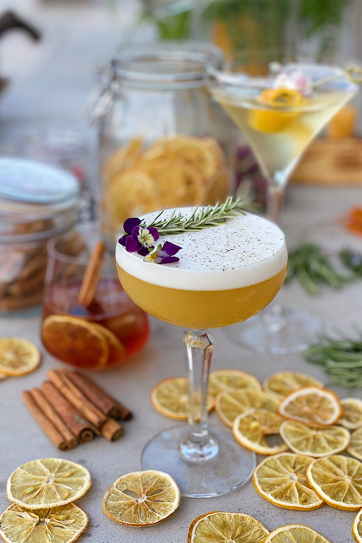 a foamy yellow cocktail in a coupe glass garnished with an edible flower and surrounded by lemon slices