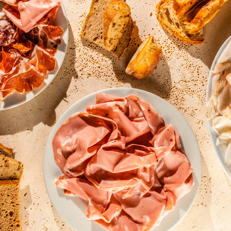 three plates of cured meats and some bread sitting on a tan concrete table