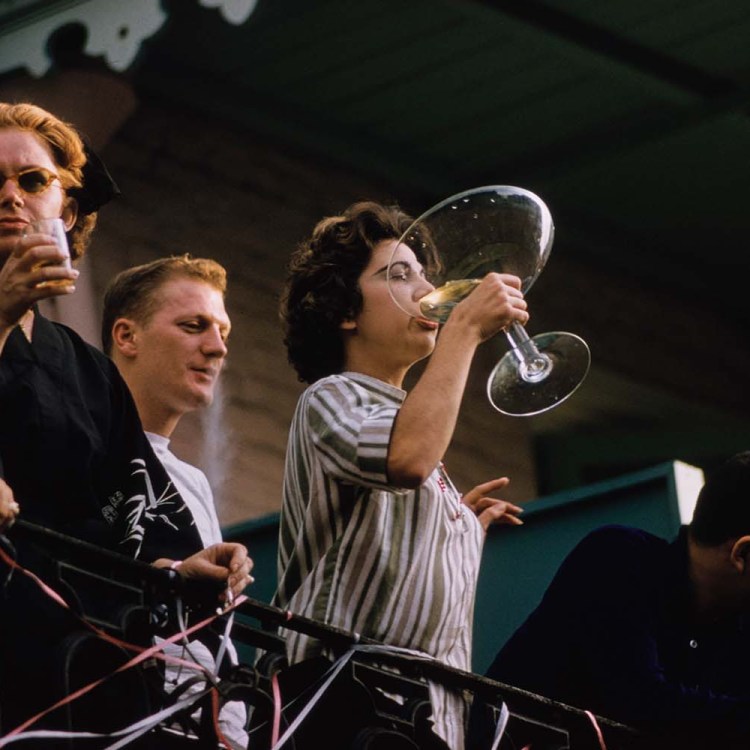 A young woman on a balcony, drinking from an outsize champagne coupe during Mardi Gras in New Orleans, Louisiana, 1961