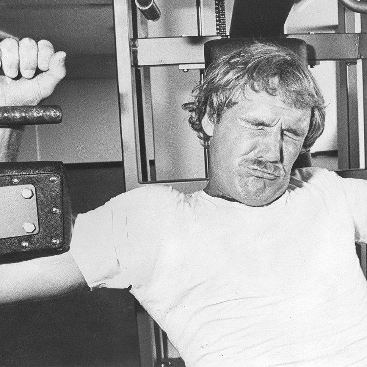 A tired man struggles to push a weighted machine at the gym. Black and white photo.