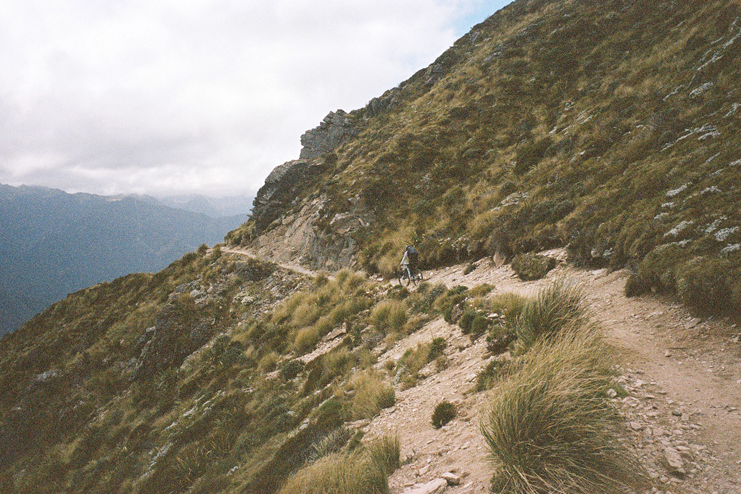 A cyclist hugs a cliff with the sky in the background.