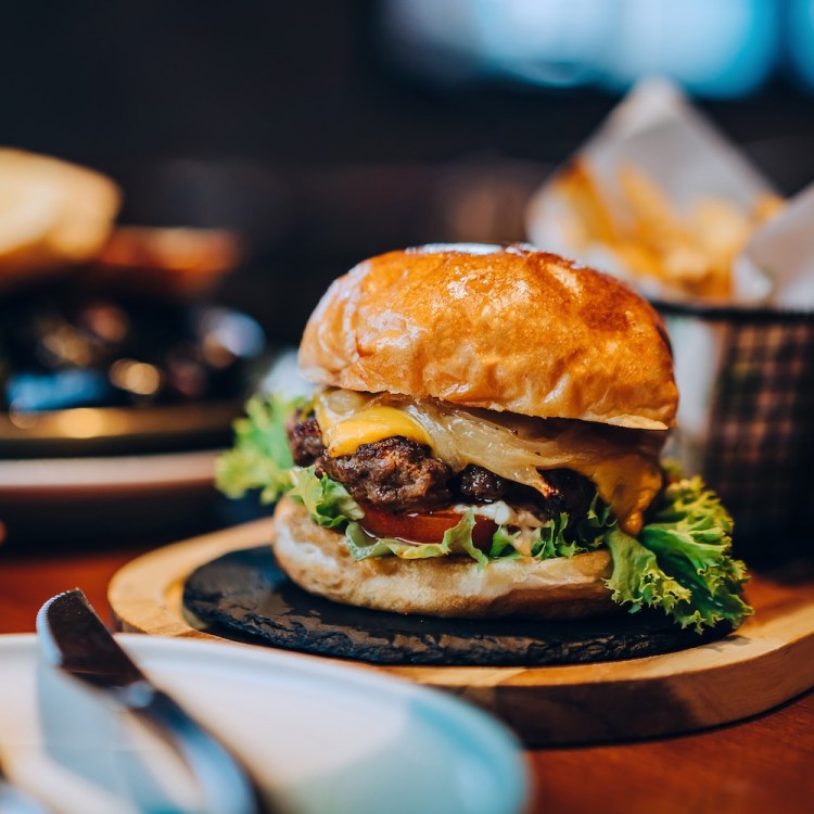 Fresh delicious burger with french fries and salad served on rustic wooden board on table. A feast on the dining table in restaurant. Food and lifestyle concept