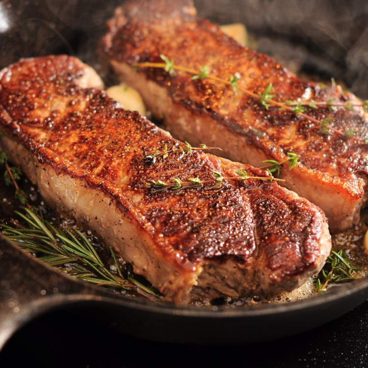 Two strip loins pan seared in a cast iron pan with herbs and garlic